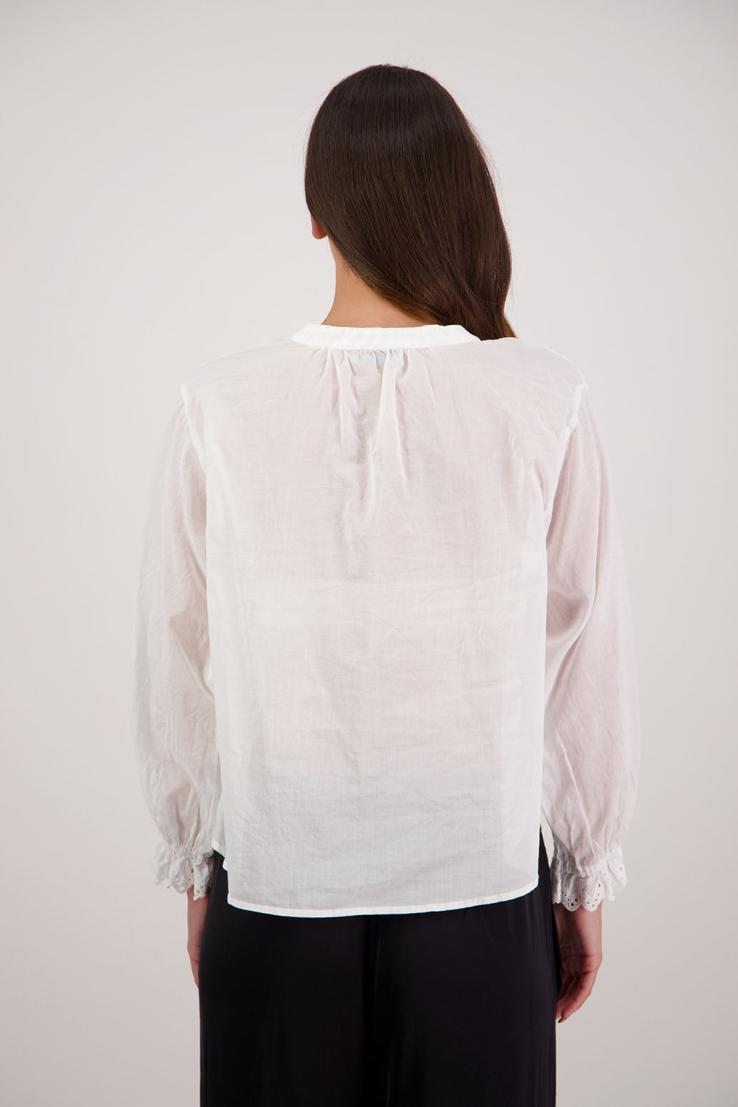 Woman wearing a Randall white shirt with long sleeves against a plain background. Subtle embroidered sleeves.