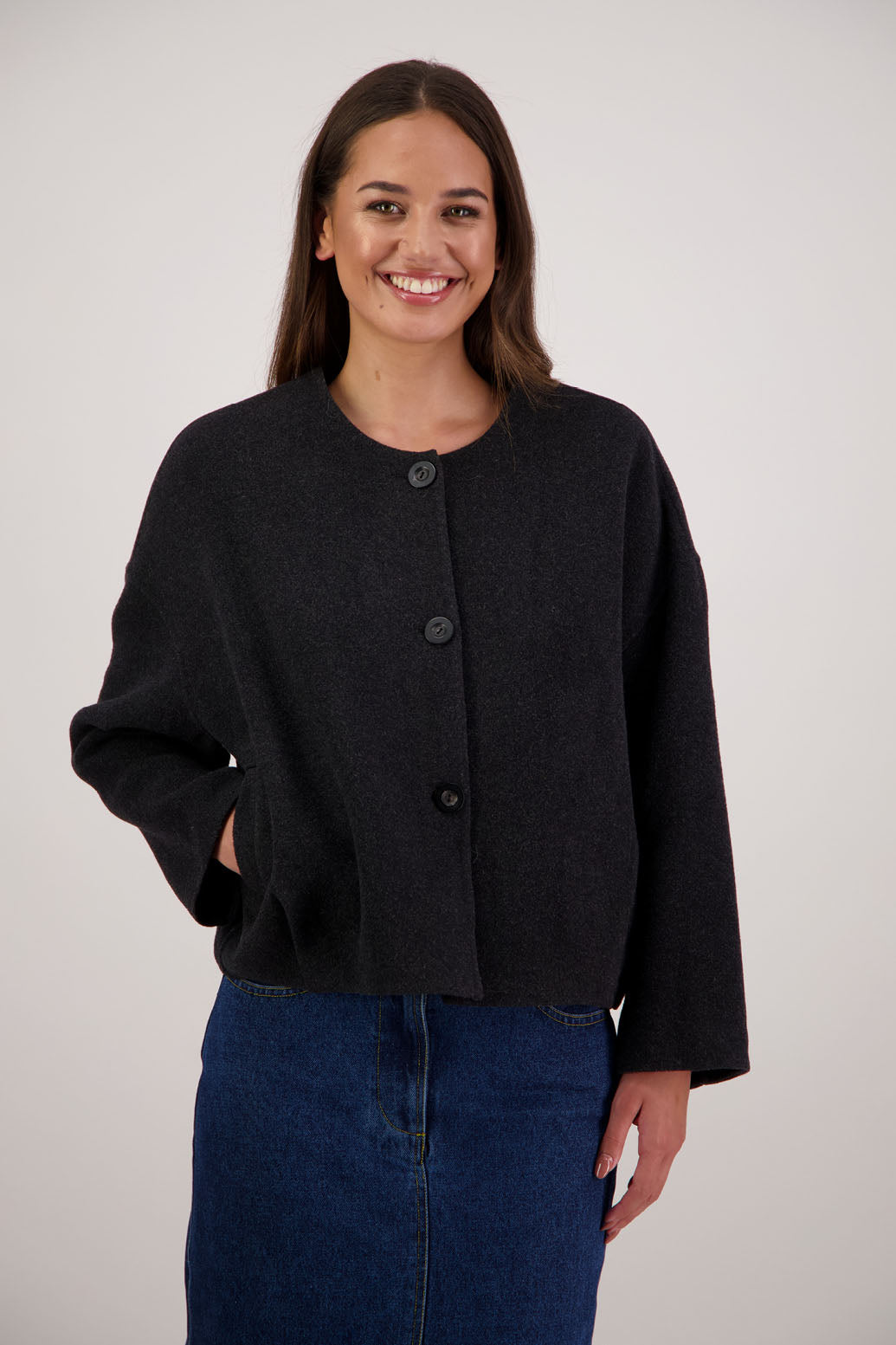 Renee Jacket in Black by Briarwood NZ. Features, no collar, button closure, shaped sleeves, pockets, drop shoulder and dart type pleats on the hem of the jacket